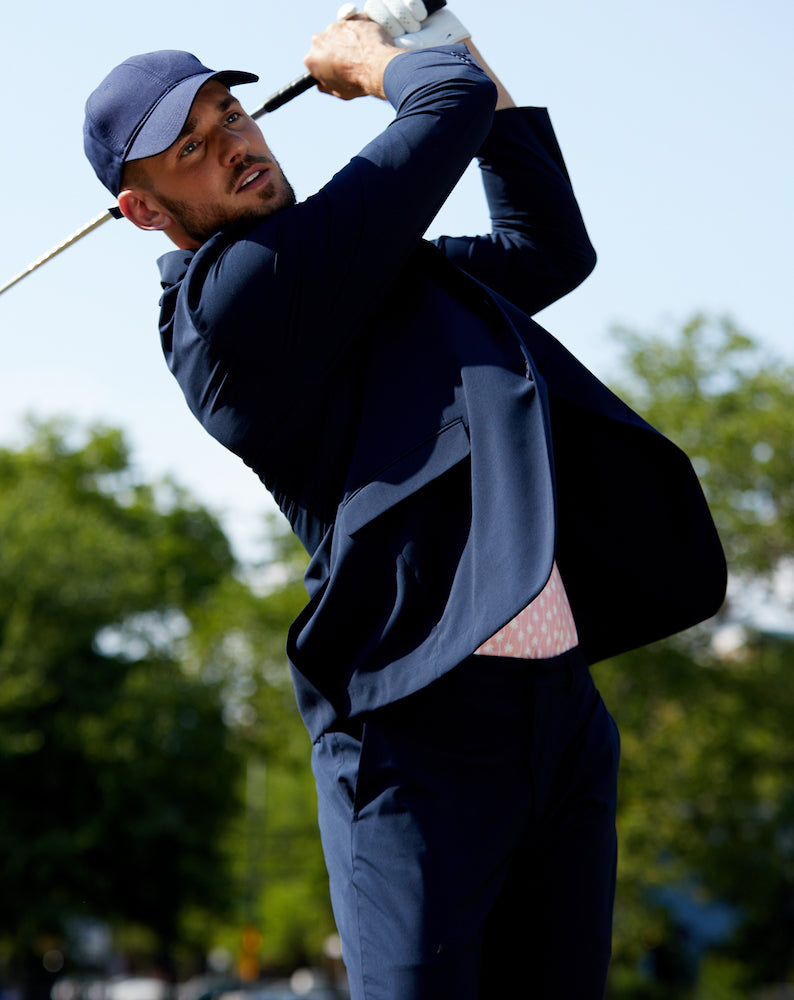 Man in a navy blue baseball cap playing golf in a State of Matter's Navy Cooling Performance Suit Jacket and sustainable men's navy suit pants