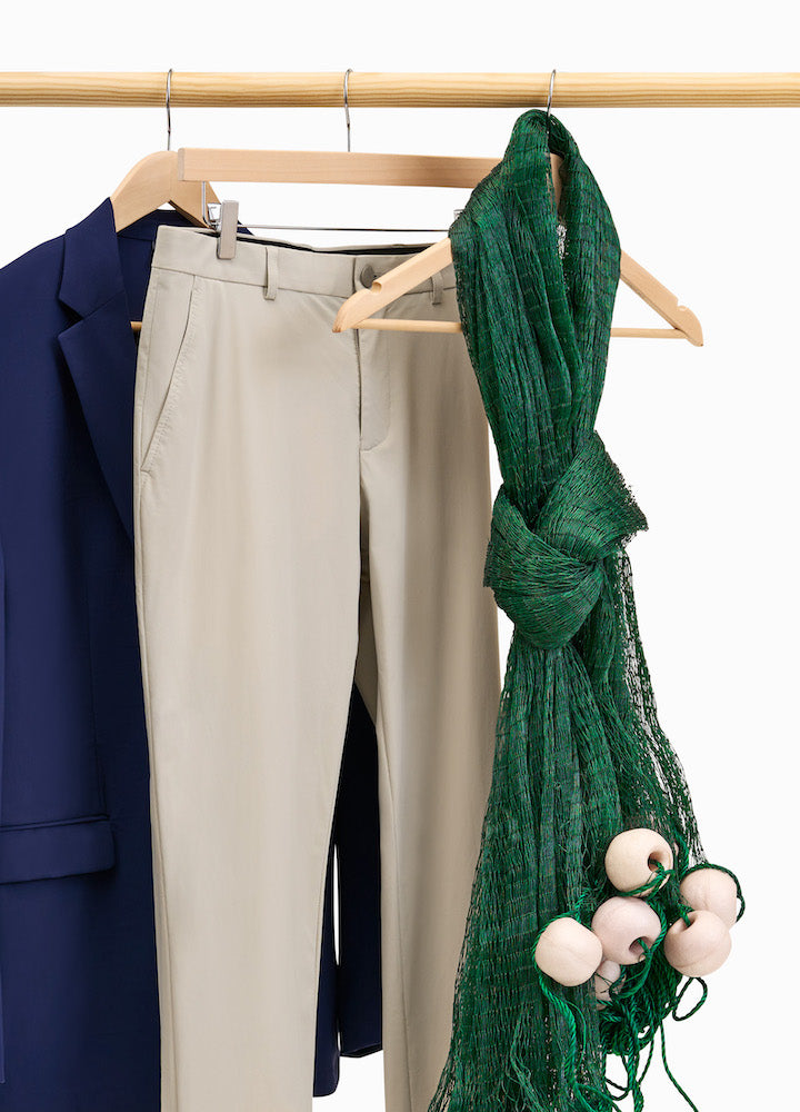 A clothing rack with the State of Matter navy suit on a hanger next to a pair of sustainable men's khaki chino pants and an olive green scarf 