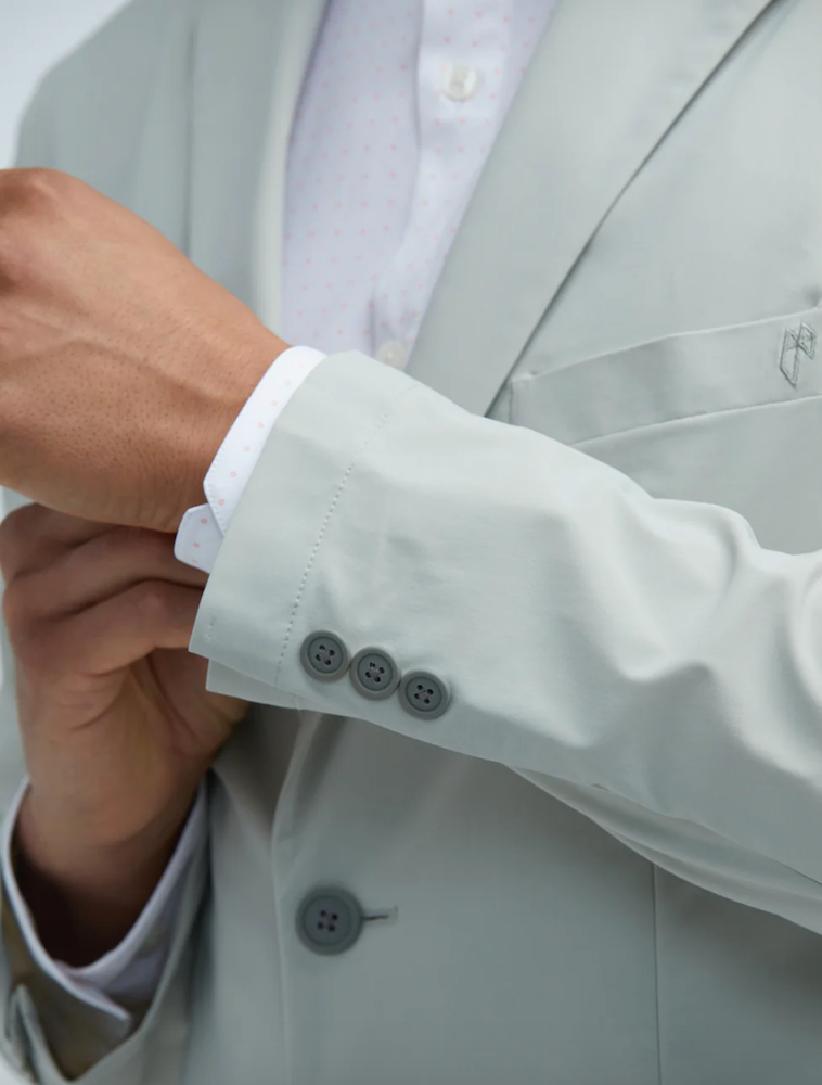 Close-up of a man fixing his sustainable shirt sleeve in a grey State of Matter suit with a men's white long sleeve button down 