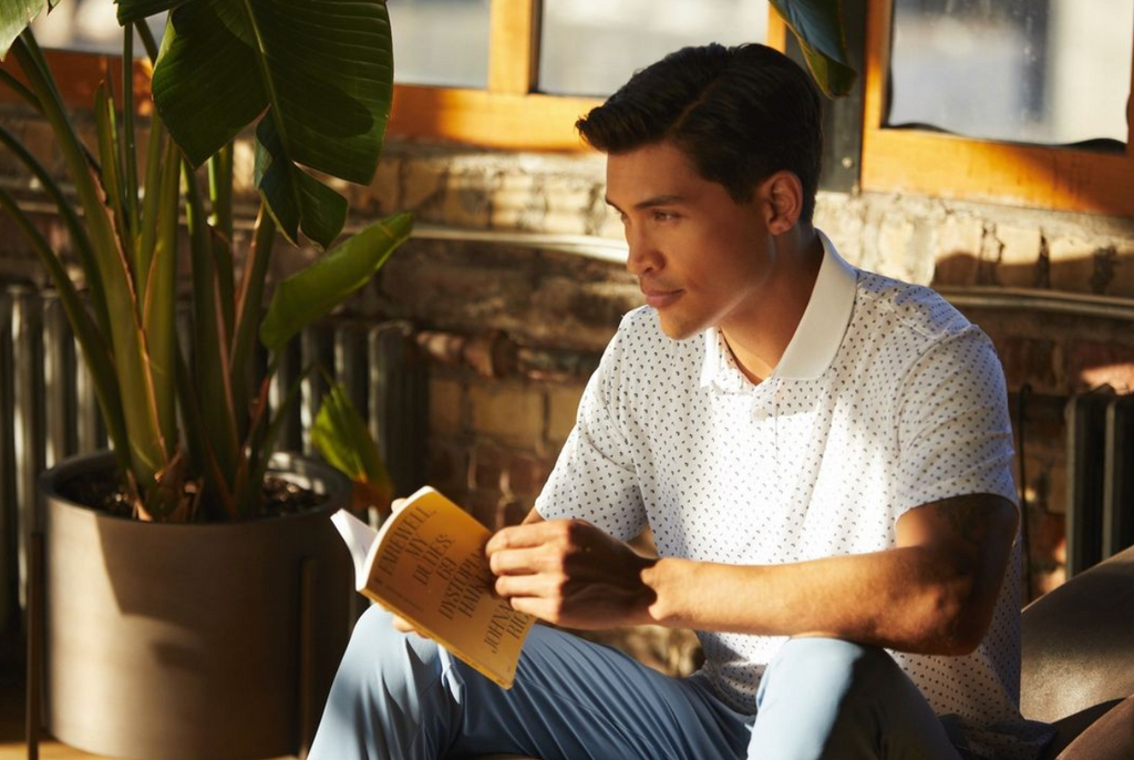 A man sitting and reading a book wearing a State of Matter Men's Baby Blue Polo Shirt