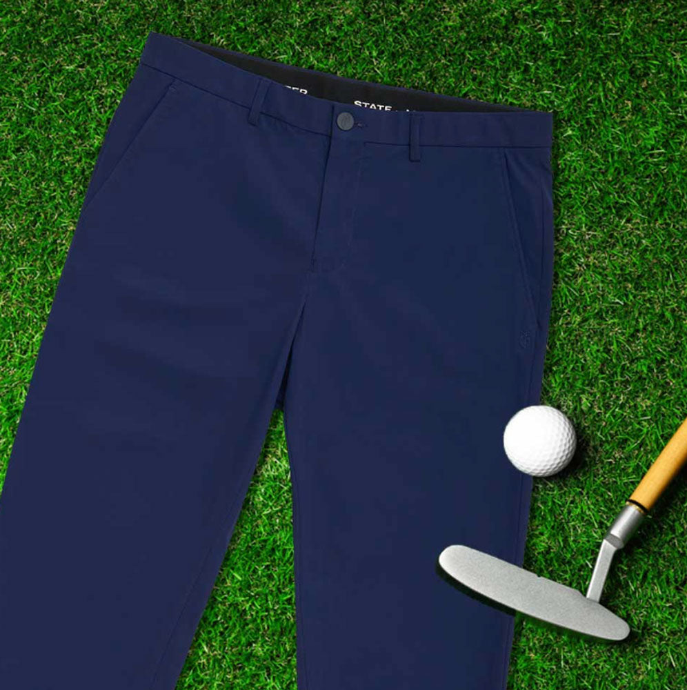 A pair of men's State of Matter navy chino pants laid out on green grass next to a golf ball and golf club