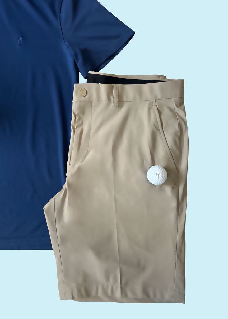 A golf ball and State of Matter sustainable navy polo shirt and men's khaki shorts against a light blue backdrop 