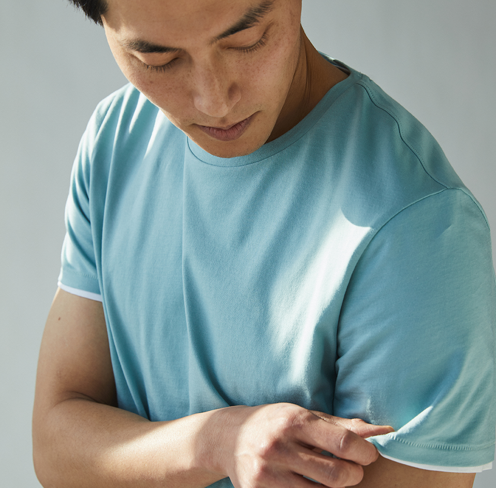 Close-up of a man wearing a teal T-shirt layered over a state of matters white sustainable plain T-shirt, focusing on the details and fabric.