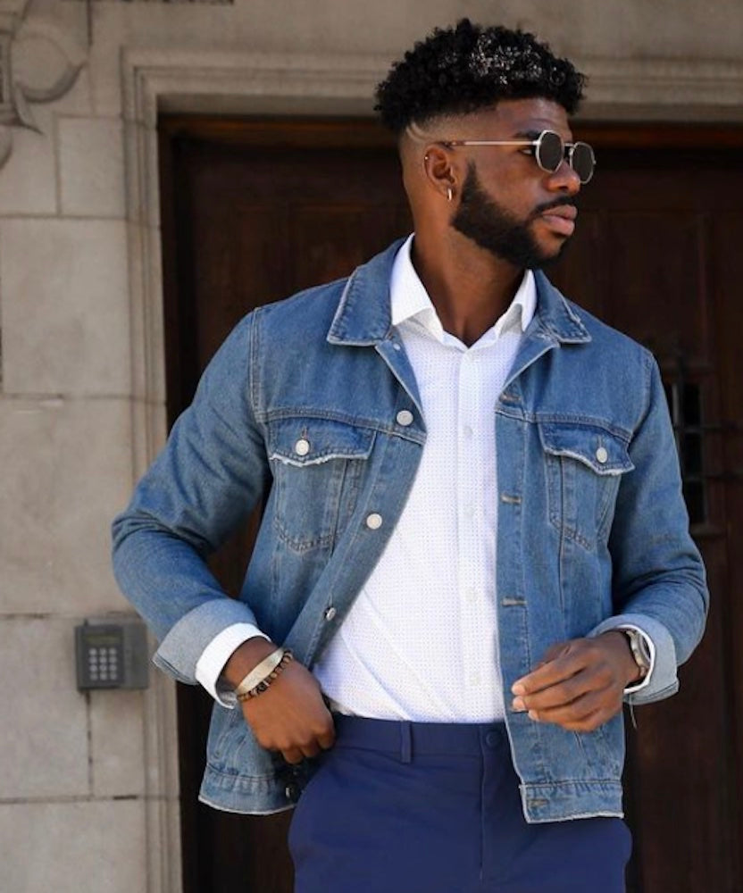 A man in sunglasses looking away rom the camera is wearing a denim jacket and State of Matter white button down tucked into a pair of sustainable navy pants. 