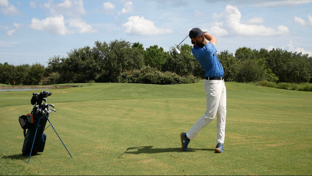 A bearded man playing golf on a golf course in a pair of State of Matter sustainable light grey chino pants 