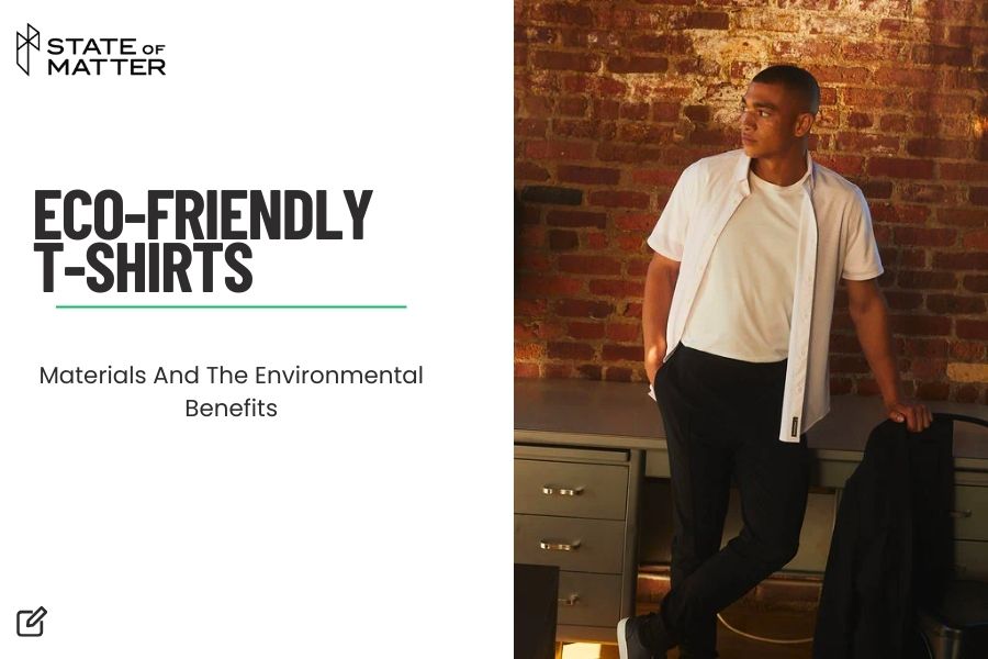 Man in an eco-friendly white T-shirt and black pants posing in a room with a brick wall, for a blog about the environmental benefits of sustainable clothing.