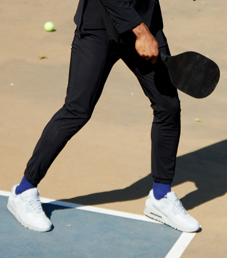 The bottom half of a man on a racquetball court wearing State of Matter black joggers and white Tennie shoes.