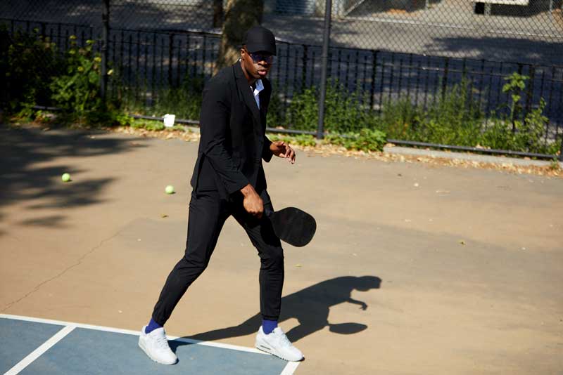 Man playing pickle ball while wearing Stata matters men sustainable black suit jacket and black joggers