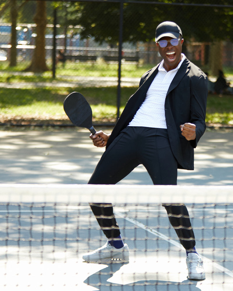 A man celebrating a game of racquetball wearing a Sate of Matter black Cooling Performance Suit. 