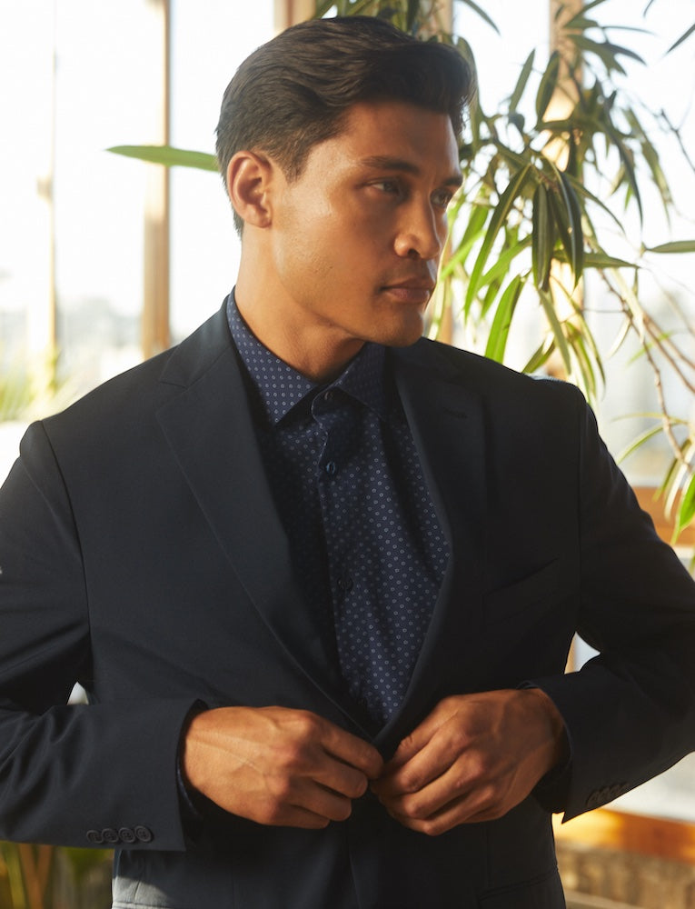 A man looking away from the camera buttoning up his State of Matter black Men's Suit Jacket over a sustainable Men's Deep Navy Flower Long Sleeve Dress Shirt. 